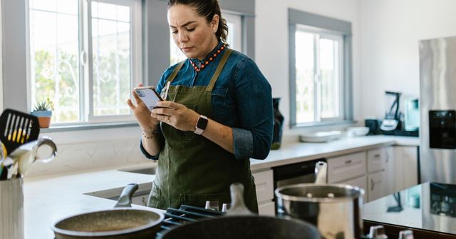Personne en tablier consultant une recette sur son téléphone dans une cuisine lumineuse